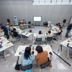 Estudantes participam de uma oficina prática em sala de aula, utilizando equipamentos tecnológicos.