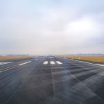 Pista de aeroporto vazia se estende ao longe sob céu enevoado.