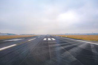 Pista de aeroporto vazia se estende ao longe sob céu enevoado.