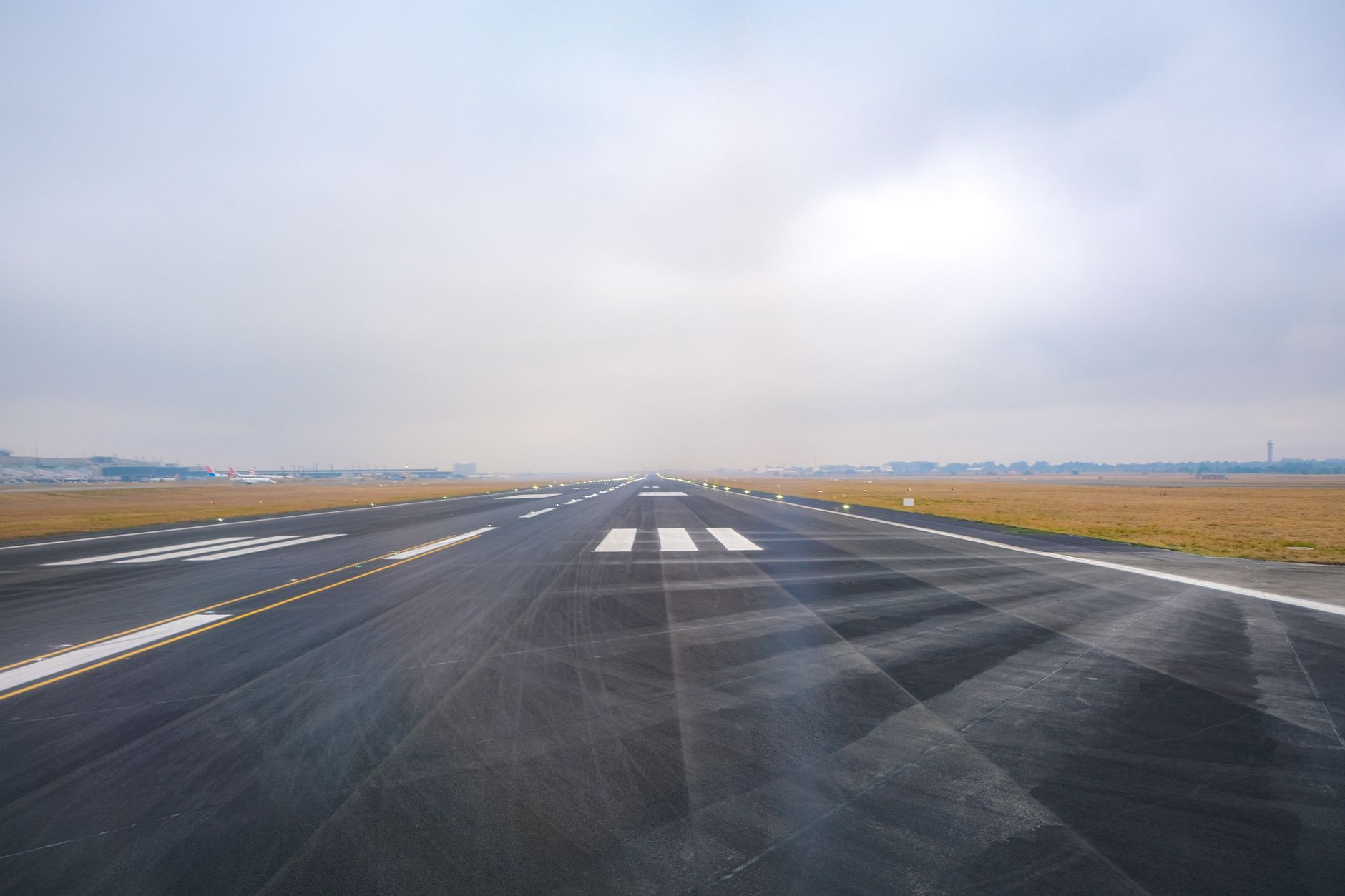 Pista de aeroporto vazia se estende ao longe sob céu enevoado.